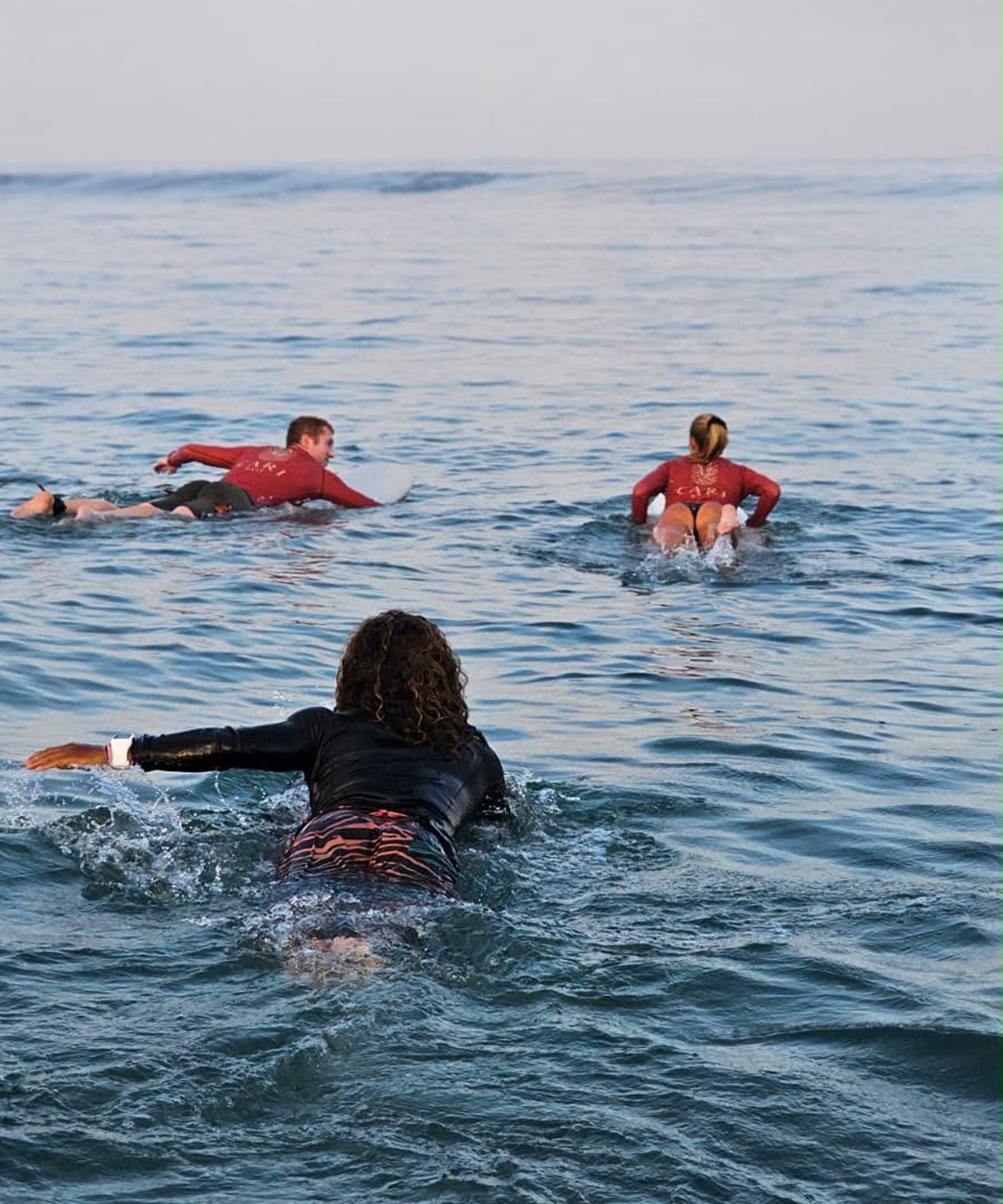 Three surfers paddling out into ocean waves